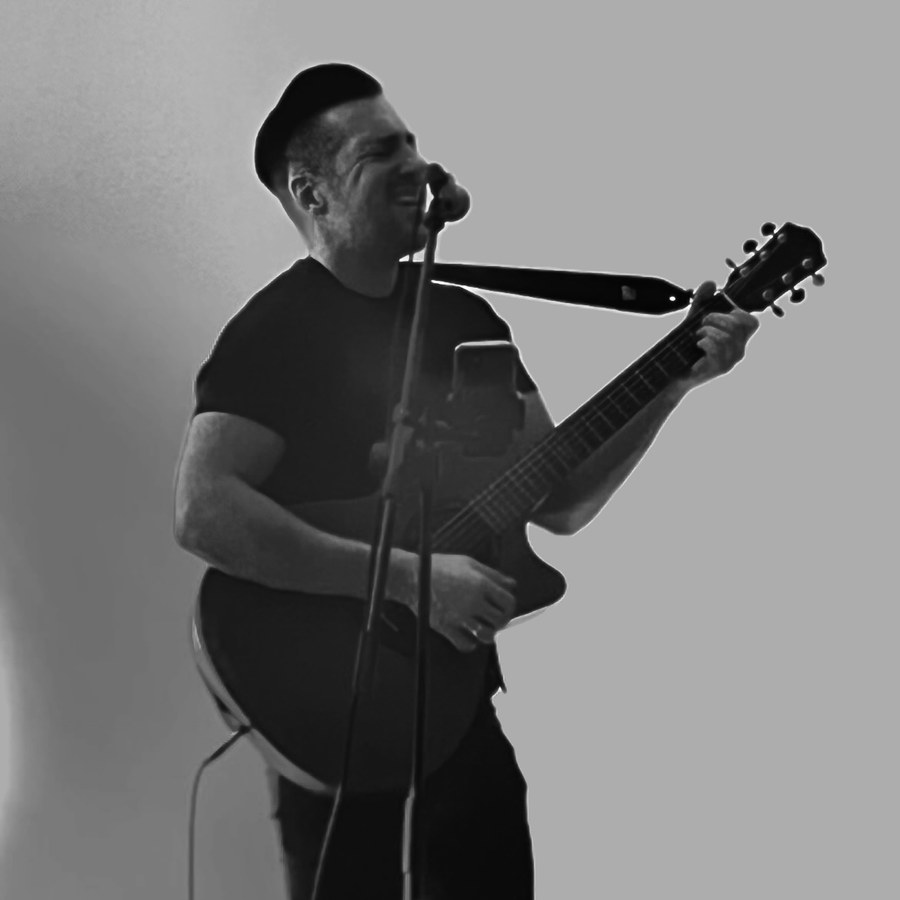 Jenson beim Live-Gesang mit Mikrofon und Gitarre auf der Bühne